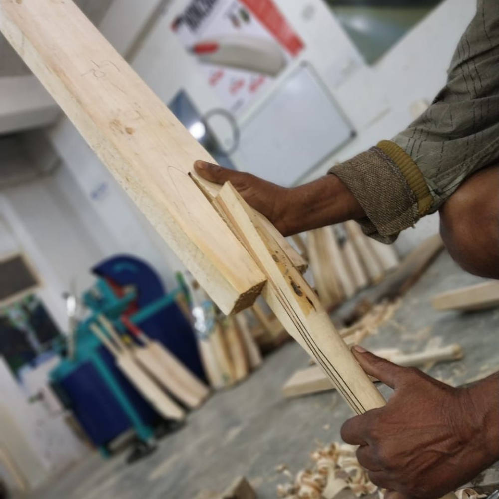 Close-up of a woodworker's hands planing a thin wooden board in a cluttered workshop.